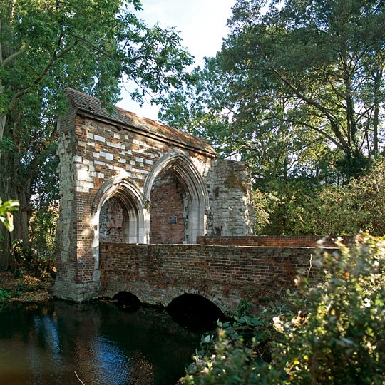 The gatehouse in dappled shade with adjoining bridge arching over the Cornmill Stream