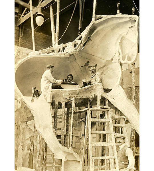 Adrian Jones and his assistants - Jones and two assistants are sat inside one side of the casting moulds of a Quadriga horse, taking tea at a low table. The sculpture was to later be erected onto Wellington Arch.