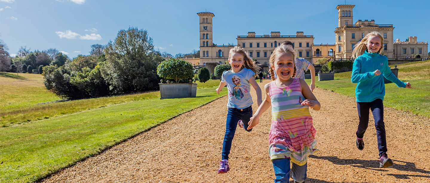 Three children run joyfully in front of a large palatial house with towers