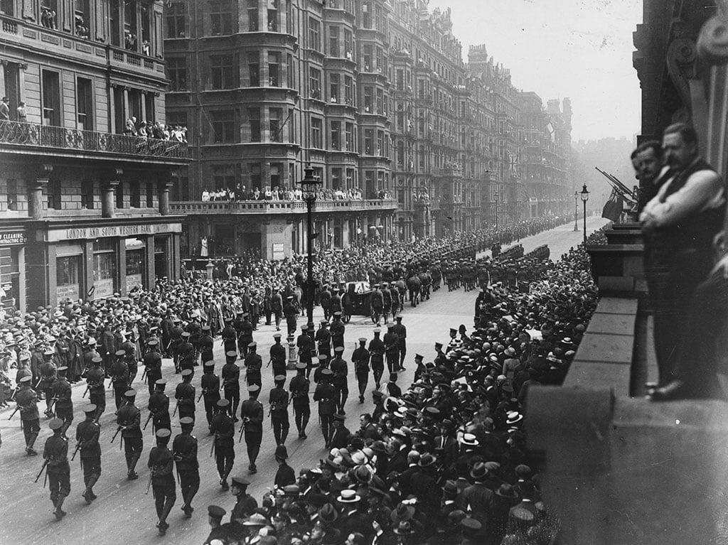 A black and white image of a large funeral procession going down a central London street lined with hundreds of onlookers