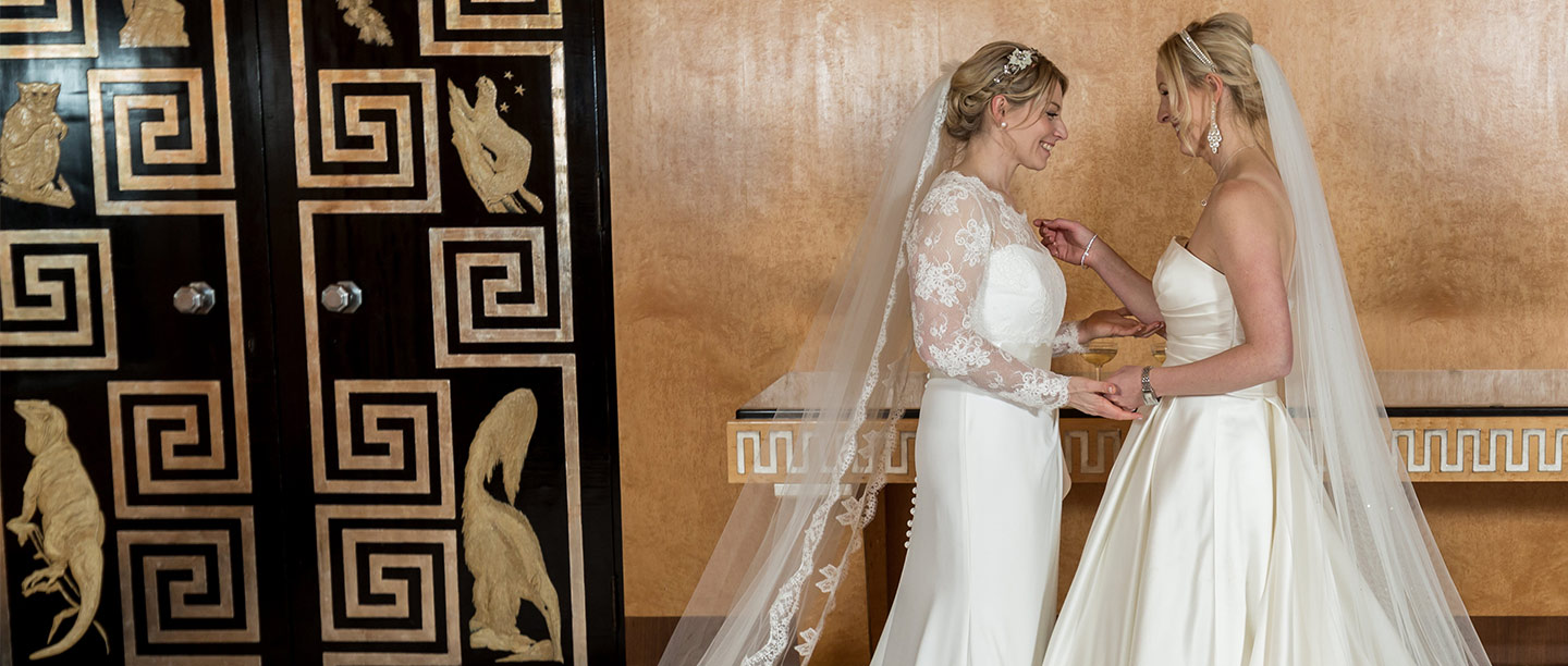 Two women in white wedding dresses look lovingly at each other