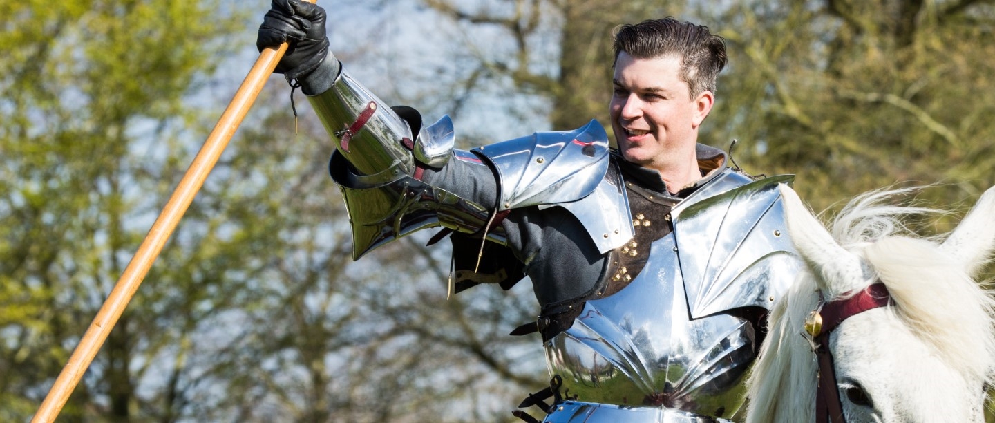 Photo of a person in knight's armour riding a horse and holding a flag
