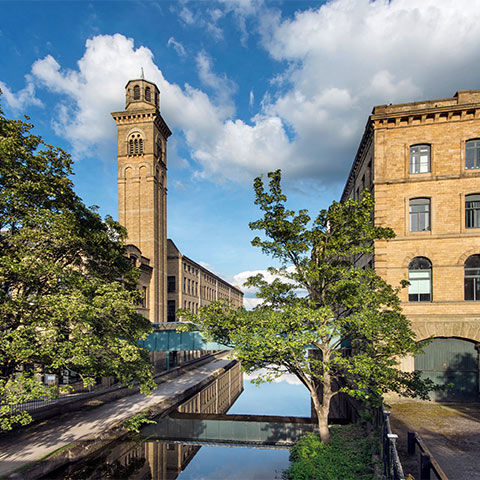 A canal runs between a mill building and a tower in Saltaire
