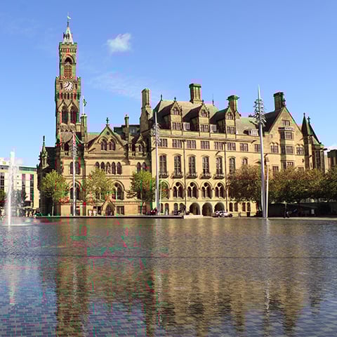 A large building (Bradford Town Hall) stands the other side of a pool of water