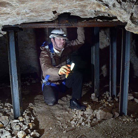 A man with a hard hat crouches in a low cave or tunnel