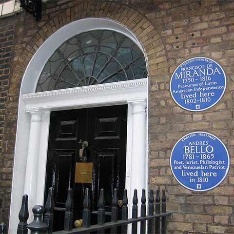 A doorway with two blue plaques dedicated to Francisco de Miranda and Andres Bello on the exterior wall.