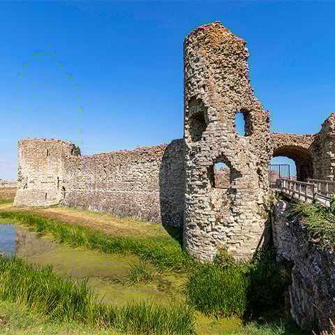 A view of Pevensey Castle stone walls and tower on a sunny day.