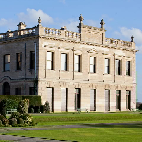 A side on view of Brodsworth Hall underneath a blue sky.