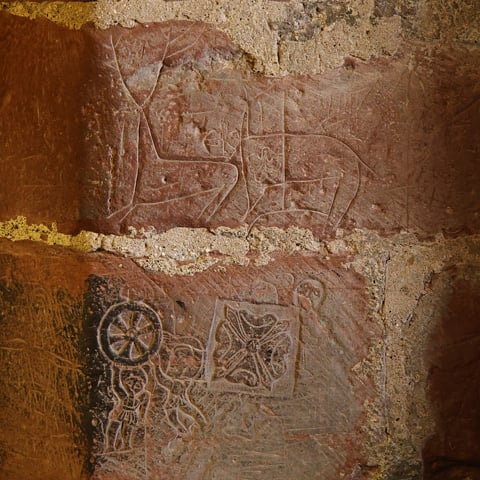 A close-up view of the stone walls at Carlisle Castle featuring historic graffiti, depicting images of deers and decorative flower symbols.
