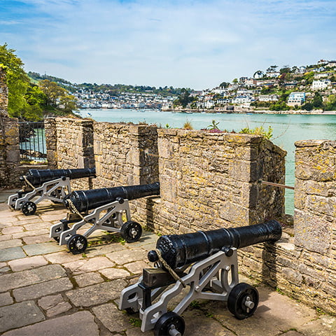 Cannons poke through battlements on a castle wall looking across a river estuary