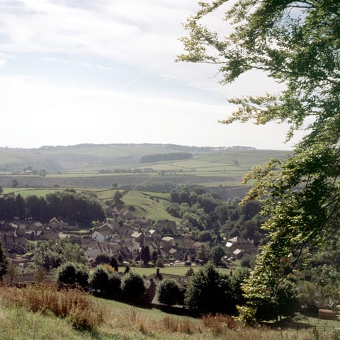 A view from the hills looking down on the village of Eyam, which is surrounded by fields and greenery.