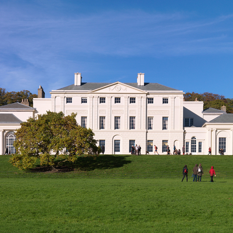 A view of the facade of Kenwood House with people walking in front of the building. 
