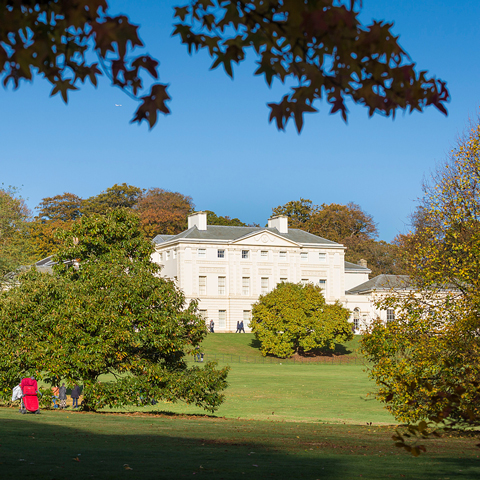 A view of Kenwood House through the trees, underneath a blue sky.