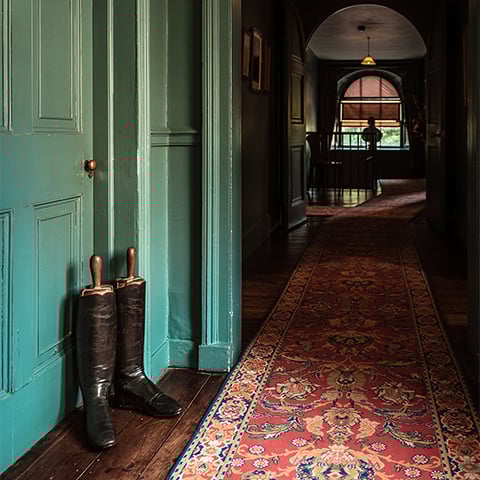 A corridor in a grand building with a pair of boots by a green door