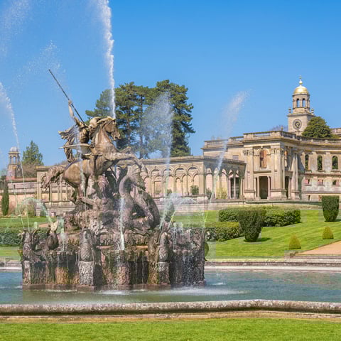 A view of Witley Court ruins on a sunny day and the water fountain in the foreground.