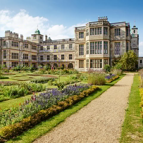 A view of Audley End House underneath a blue sky overlooking the gardens with rows of colourful flowers.