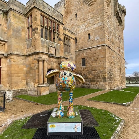A large painted colourful statue of Shaun the Sheep standing in front of Belsay Castle.