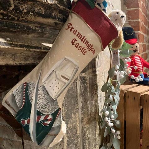 A Christmas stocking hung on a fireplace with the words 'Framlingham Castle' stitched in red.