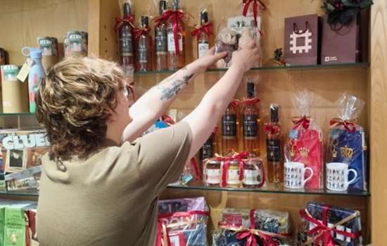 Someone in English Heritage uniform is stacking Christmas themed products on shelves in a gift shop. Someone in English Heritage uniform is stacking Christmas themed products on shelves in a gift shop.