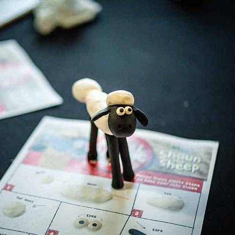 A small clay Shaun the Sheep figure stands on an instruction leaflet.