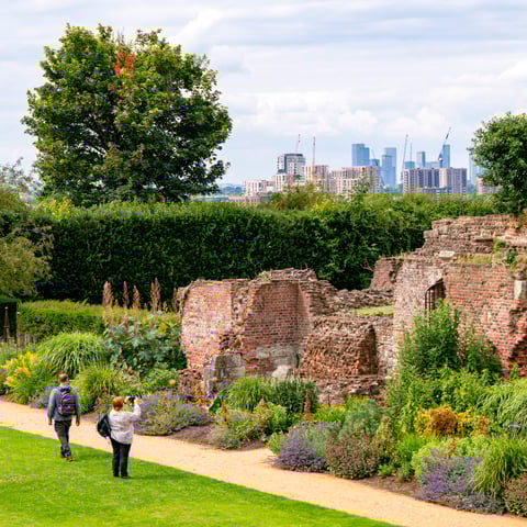 Two adults stand beside the brick walls in the gardens at Eltham Palace with view of a section of London's skyline in the background.