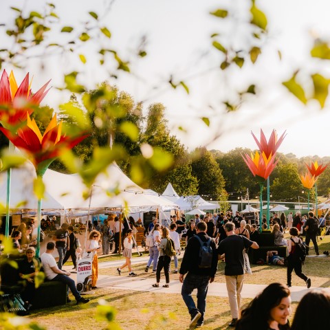 An outdoor festival with crowds of people walking among large white tents and sculptures of flowers. 
