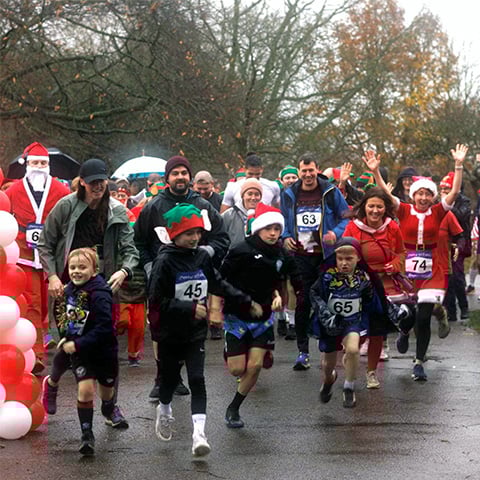 A group of runners start a race, some wearing Santa hats, on a rainy, wintry day