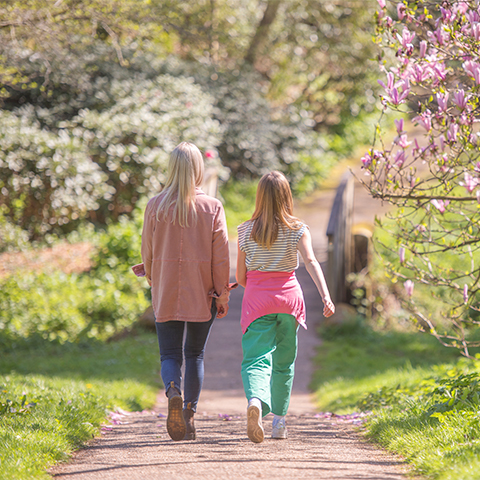 Two women walk away from the camera down a garden path