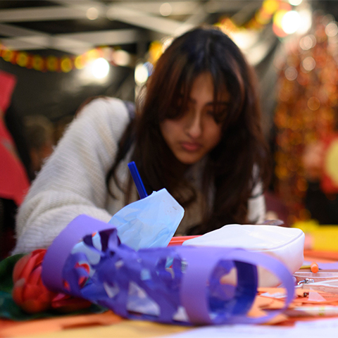 A young woman sits at a table crafting with pens and pieces of paper folded into lantern shapes