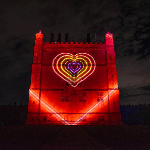 Bolsover Castle is lit up at night with large red projections with large glowing colourful hearts projected on the centre of the building. 