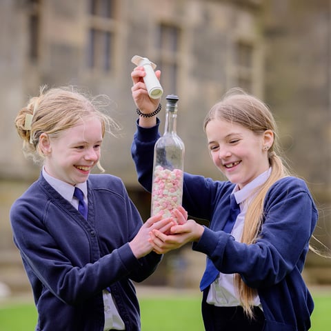 Two children in blue school uniforms hold a glass bottle filled with marshmallows at Bolsover Castle. 