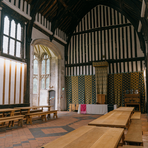The interior of a timber-framed medieval hall with tapestries hung on the wall.