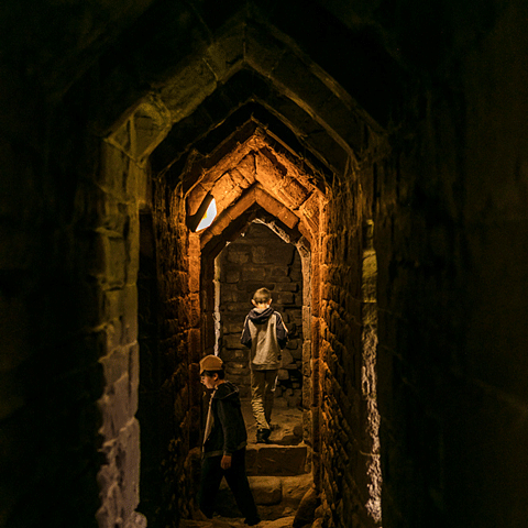 A dimly lit stone castle tunnel with two young children through them.  A dimly lit stone castle tunnel with two young children through them.
