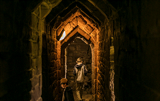 A dimly lit stone castle tunnel with two young children through them.  A dimly lit stone castle tunnel with two young children through them.