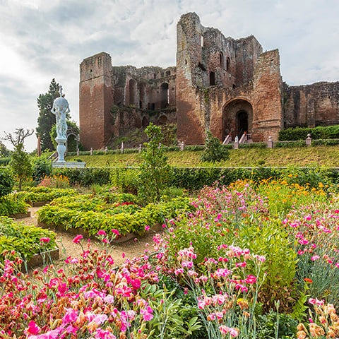 Pink flowers bloom in an ornate garden with the ruin of a castle (Kenilworth) behind