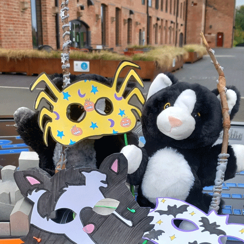 Two toy cats are surrounded by colourful Halloween themed masks outside of Shrewsbury Flaxmill Maltings.