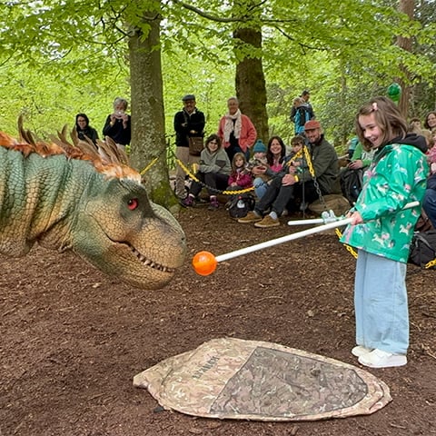A girl holds out a stick for an animatronic dinosuar to sniff 