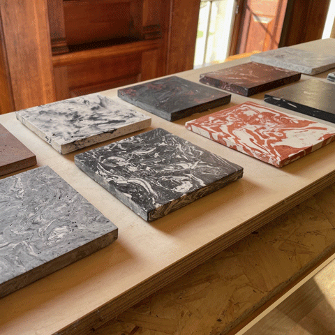 Several variations of square coloured marble slabs are laid flat on a wooden table.