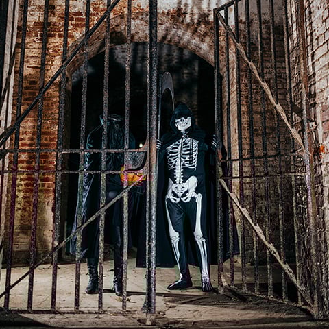 Re-enactors dressed as a headless ghost and the Grim Reaper stand in a brick gateway with an iron gate