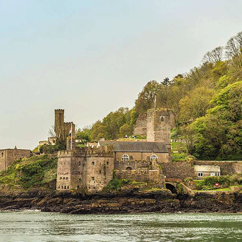 A castle perched on a hill overlooks the sea under a clear blue sky.