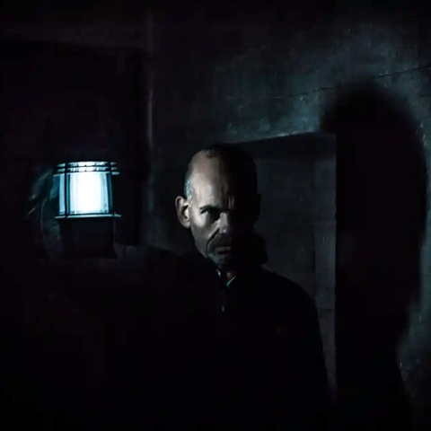 A man holds a lit lantern in a dark stone room.