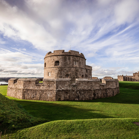 The circular stone fortress of Pendennis Castle with a central tower, surrounded by grass and under a partly cloudy sky
