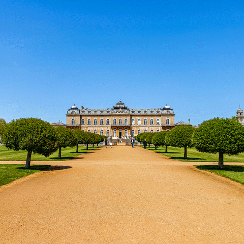 An exterior view of Wrest Park underneath a bright blue sky and rows of trees. 