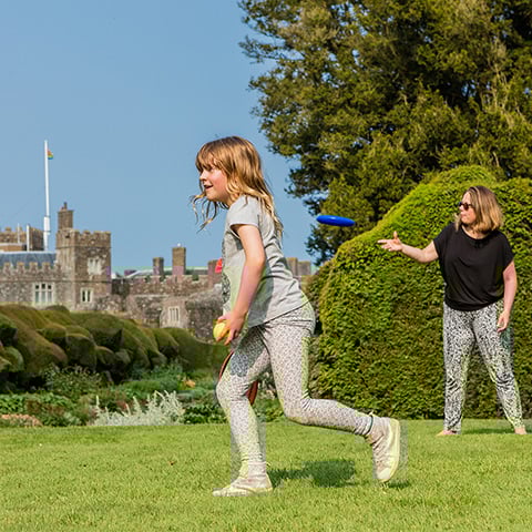 A girl and woman play with a frisbee with Walmer Castle in the background