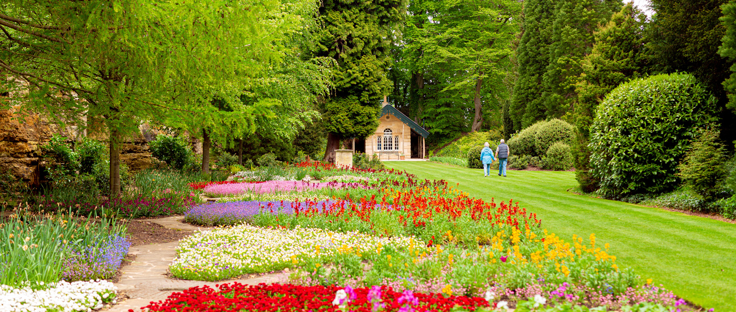 Two people stroll through the colourful flower beds in the gardens at Brodsworth Hall.
