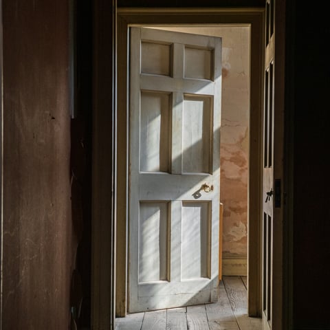 A photograph of a dimly lit hallway, with shadows on a wooden door.
