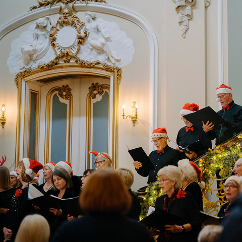 An adult choir perform holding songbooks while wearing Christmas hats at Wrest Park.