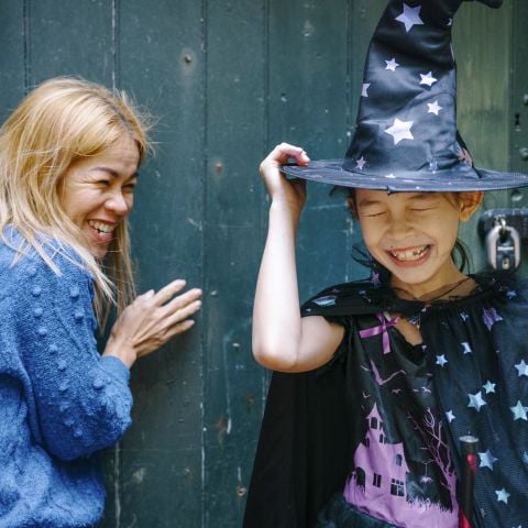 A woman laughs with a young girl wearing a witch's hat
