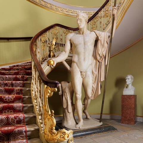 A view of the curved staircase in Apsley House with a large marble statue in the middle of the room.