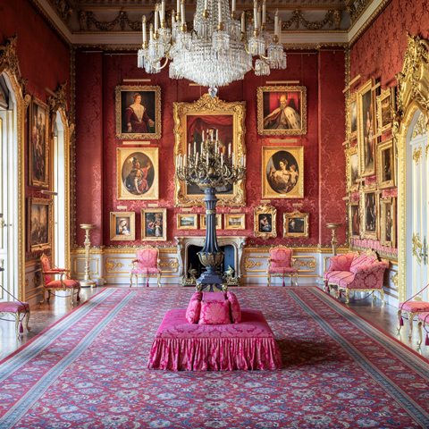 The interior of Apsley House with red patterned wallpaper, a large chandelier and paintings hung on the walls. 